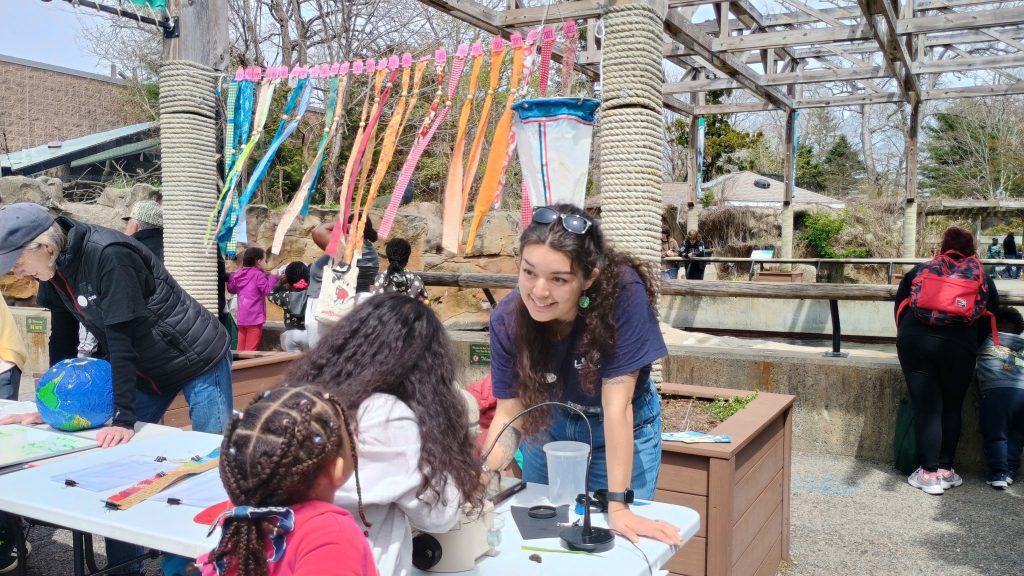 Woman talking to children looking through microscope, colored banners behind her.